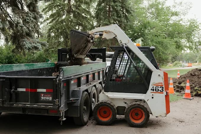 A skid steer loading soil into a dump trailer on an Alberta job site